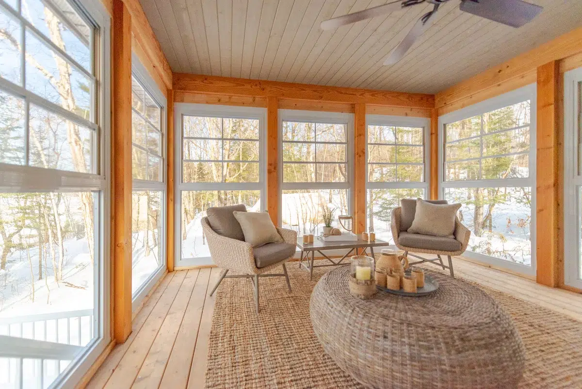 Sunroom featuring WeatherMaster™ Windows, natural wood accents, wicker furniture, and a warm, inviting ambiance with a snowy forest view.